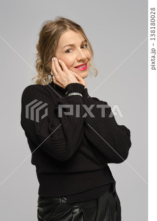 Woman in black sweater poses with a smile while holding her face with one hand indoors 138180028