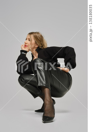 Woman poses in a crouched position wearing black clothing in a studio environment Woman poses in a crouched position wearing black clothing in a studio environment 138180035