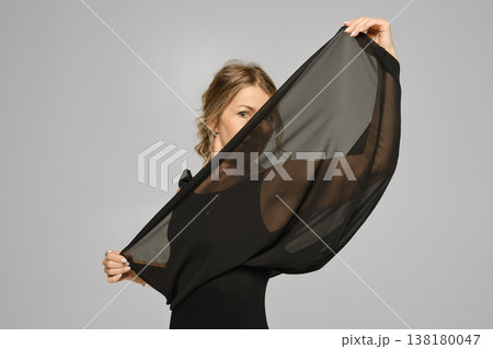 Woman holds black fabric in front of her face during indoor photo session in a studio 138180047