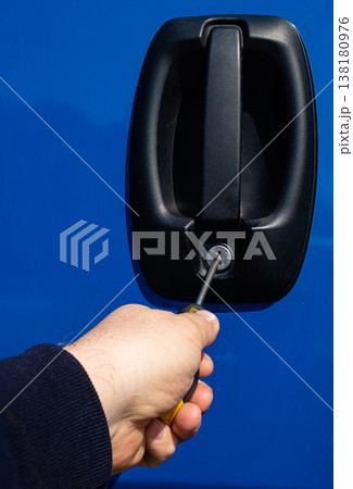 Thief using screwdriver to break into blue car door lock Thief using screwdriver to break into blue car door lock 138180976