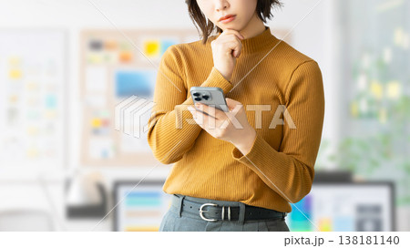 スマートフォンを見て考えごとをする女性・ビジネスウーマン スマートフォンを見て考えごとをする女性・ビジネスウーマン 138181140