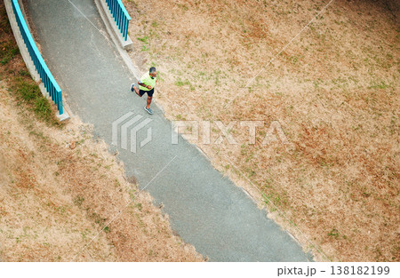 Above, man and running on path in nature, countryside or outdoor in environment with road in woods. Athlete, run or walking on street for cardio, fitness or exercise in forest with eco infrastructure 138182199