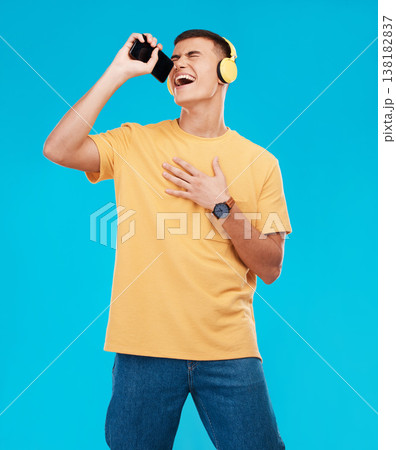 Phone, headphones and man singing in studio listening to music, radio or playlist for entertainment. Smile, technology and male person streaming song or album for karaoke isolated by blue background. 138182837