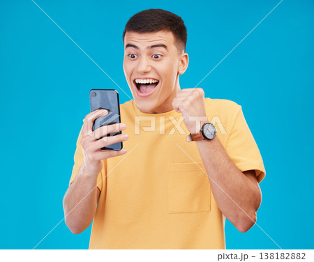 Cellphone, celebration and young man in a studio with fist pump for winning, success or achievement. Happy, smile and male winner from Canada cheering for prize on a phone isolated by blue background 138182882