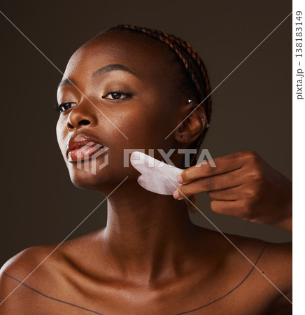 Woman, facial and gua sha in hand on studio background for mockup in beauty, treatment or skincare. Black person, model or massage for glow, lymphatic drainage or grooming with tool, relax and shine 138183149