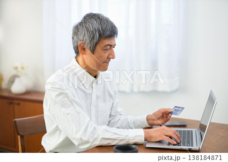 カードを見ながらパソコンからクレジット決済の手続きをするシニアの男性 カードを見ながらパソコンからクレジット決済の手続きをするシニアの男性 138184871