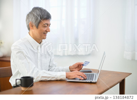 リビングでパソコンとカードを見る60代の男性 リビングでパソコンとカードを見る60代の男性 138184872