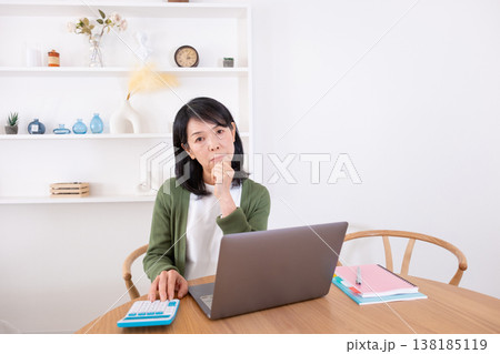 パソコンと電卓を使いながら悩む50代女性 138185119