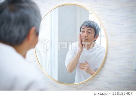 鏡を見ながら顔を手で触る60代の男性 鏡を見ながら顔を手で触る60代の男性 138185407