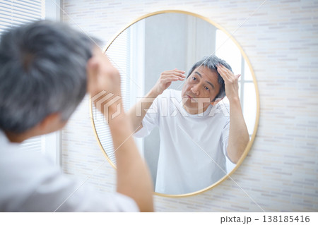 鏡を見て白髪を気にする60代の男性 138185416