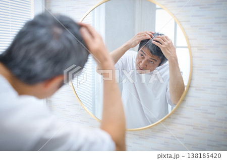 鏡を見て白髪を気にする60代の男性 138185420