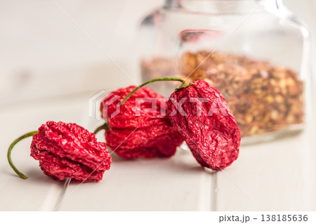 Dried Ghost Chili Peppers and Jar of Crushed Chili Flakes on White Table for Spicy Cooking 138185636