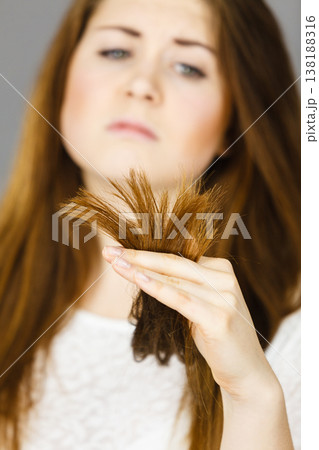 Worried woman looking at her dry hair ends Worried woman looking at her dry hair ends 138188316
