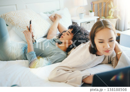 Lesbian, couple and bed with laptop and phone for streaming movie or internet for relax, connection or online. Lgbt woman, reading and lens flare home for social media or subscription in bedroom 138188508