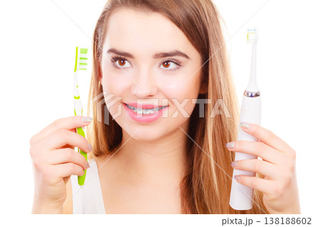 Woman with braces holding electric and traditional toothbrush 138188602