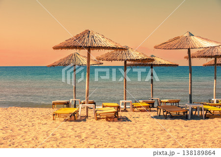Tropical beach scenery with sun parasols and evening sky. Straw sun umbrellas on the beach Tropical beach scenery with sun parasols and evening sky. Straw sun umbrellas on the beach 138189864