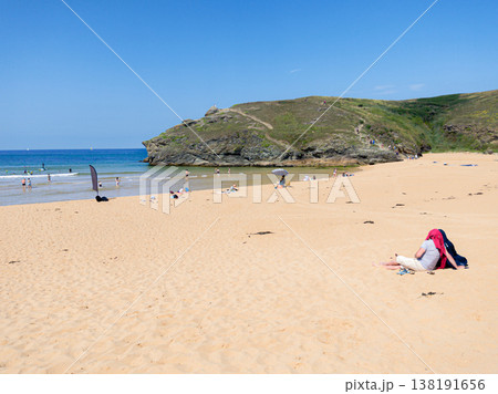 Couple Relaxing On Sandy Beach Near Rocky Headland With Swimmers And Clear Blue Sea On A Sunny Summer Day Couple Relaxing On Sandy Beach Near Rocky Headland With Swimmers And Clear Blue Sea On A Sunny Summer Day 138191656