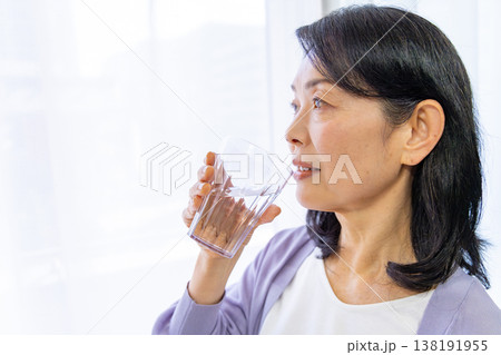 窓辺で水を飲むシニア女性 138191955