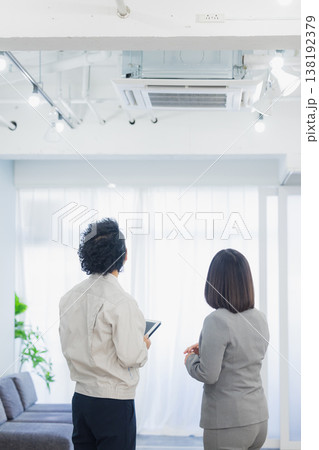 エアコンを見て不満そうな表情のビジネスウーマンと作業員　 138192379