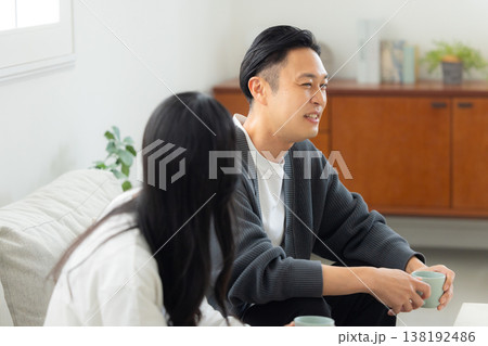 ソファーに座ってスマホを見る夫婦　 138192486