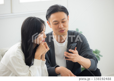 ソファーに座ってスマホを見る夫婦　 138192488