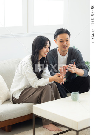 ソファーに座ってスマホを見る夫婦　 138192490