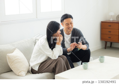 ソファーに座ってスマホを見る夫婦 ソファーに座ってスマホを見る夫婦 138192491