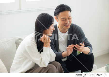 ソファーに座ってスマホを見る夫婦　 138192492