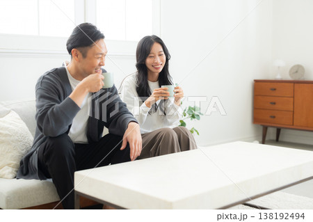 ソファーに座ってスマホを見る夫婦　 138192494