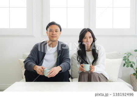 ソファーに座ってスマホを見る夫婦　 138192496