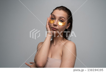 Young woman applying gold eye patches to her under-eye area, focusing on beauty, hydration, and a relaxing self-care routine for glowing, healthy skin 138194195