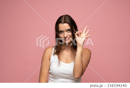 Young brunette woman making an ok gesture, expressing agreement, satisfaction, and success with a friendly smile 138194240