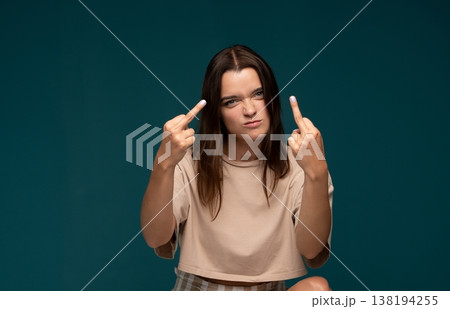 Young woman showing middle finger gesture, expressing anger, defiance, and negativity on teal backdrop Young woman showing middle finger gesture, expressing anger, defiance, and negativity on teal backdrop 138194255