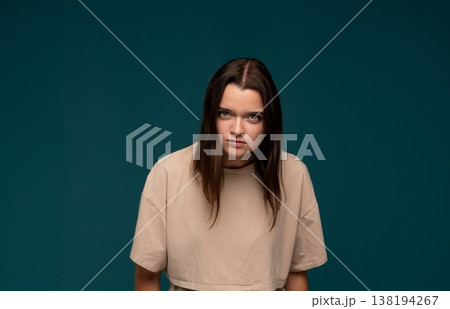 Young woman expressing anger and frustration, frowning intensely with a serious face on a blue background Young woman expressing anger and frustration, frowning intensely with a serious face on a blue background 138194267