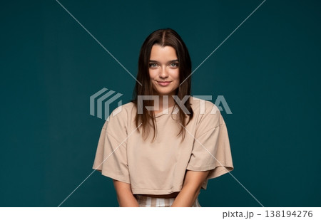 Smiling young woman posing with confidence against a turquoise background, feeling happy and casual 138194276