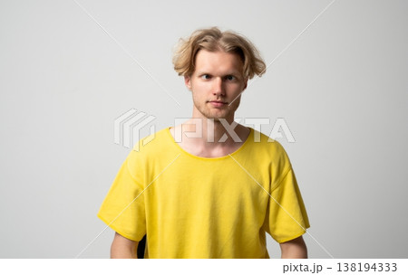Young blond man with messy hair and yellow t-shirt making a silly cross-eyed facial expression, showing playful mood and humor on a studio background Young blond man with messy hair and yellow t-shirt making a silly cross-eyed facial expression, showing playful mood and humor on a studio background 138194333