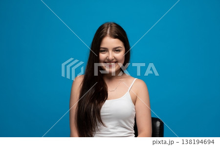 Young Caucasian woman with long brown hair smiling against a blue background, expressing happiness and joy 138194694