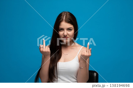 Young woman showing middle finger gesture, expressing aggression and defiance on a blue background Young woman showing middle finger gesture, expressing aggression and defiance on a blue background 138194698