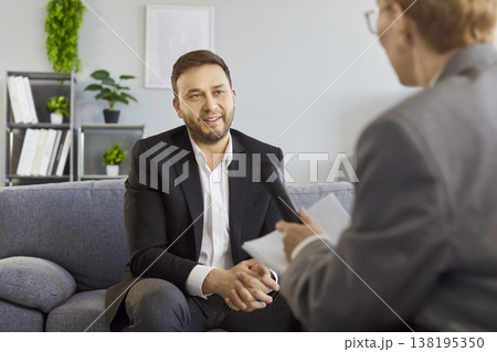 Businessman speaking in interview on sofa, interviewer with microphone in office Businessman speaking in interview on sofa, interviewer with microphone in office 138195350