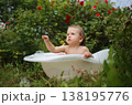 A girl in a picturesque garden in a small white bath catches soap bubbles among the flowers. 138195776
