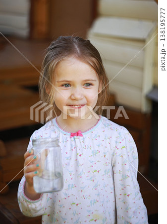 A village girl drinks water from a jar and smiles. 138195777