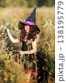A girl in a black dress and a witch's hat collects herbs for a potion.  138195779