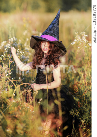 A girl in a black dress and a witch's hat collects herbs for a potion. A girl in a black dress and a witch's hat collects herbs for a potion. 138195779