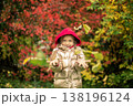A girl in a gold-colored jacket smiles, throws pink and yellow leaves on an autumn day 138196124