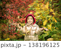 A girl in a gold-colored jacket smiles, throws pink and yellow leaves on an autumn day 138196125