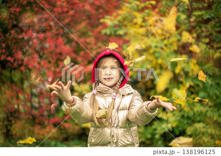 A girl in a gold-colored jacket smiles, throws pink and yellow leaves on an autumn day A girl in a gold-colored jacket smiles, throws pink and yellow leaves on an autumn day 138196125