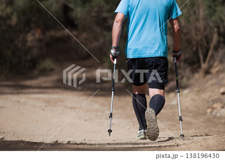 Senior man walking in forest with Nordic walking sticks, sunny summer day. An active lifestyle in retirement, a hike in nature 138196430