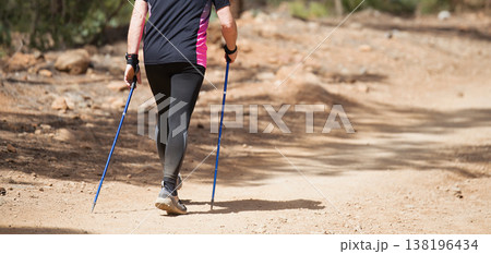 Senior man walking in forest with Nordic walking sticks, sunny summer day. An active lifestyle in retirement, a hike in nature 138196434