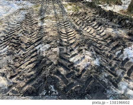 Tracks left by a vehicle in muddy ground with patches of snow in winter season 138196602
