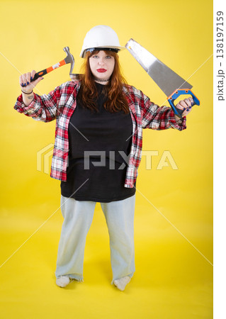 Woman holding hammer and saw on yellow background Woman holding hammer and saw on yellow background 138197159